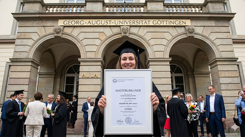 Absolventin mit Masterurkunde der Universität Göttingen vor der Aula